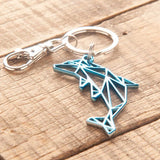 Del-Sol-Color-changing-Metal-Dolphin-Keychain--Silver-to-Blue lying on a wooden surface.