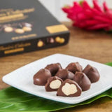 Hawaiian Host "Founders Collection" Dark Chocolate Whole Macadamias on a candy dish with one piece cut open.